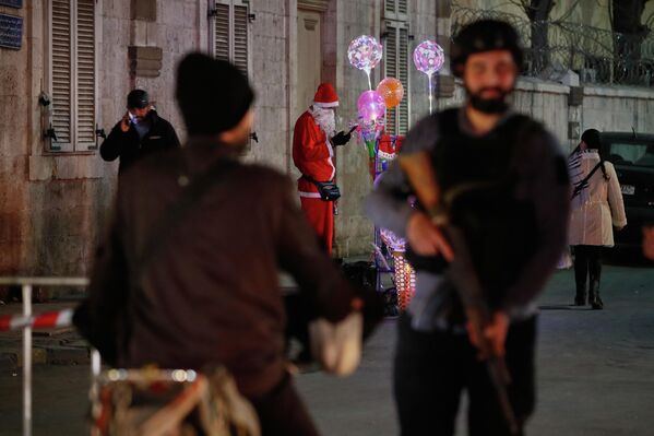 Мужчина в костюме Санта-Клауса продает рождественские украшения в христианском районе Кассаа в Дамаске, пока сирийские силы безопасности контролируют обстановку.