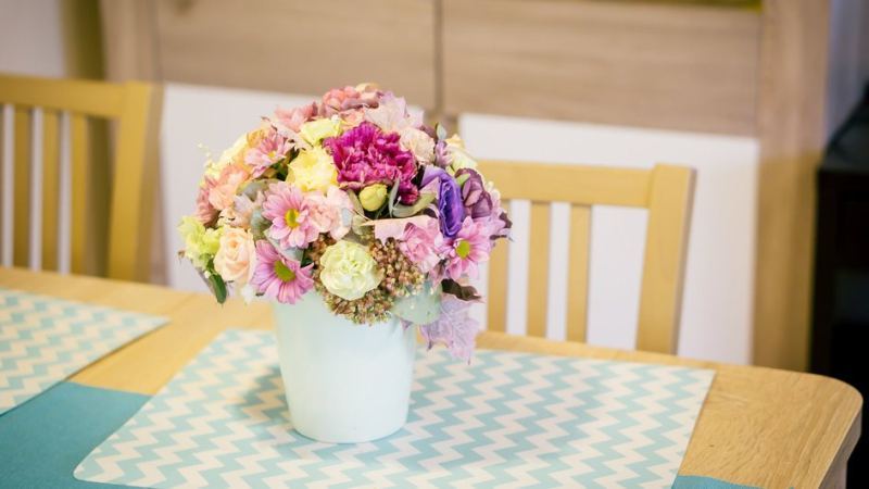 Букет сезонных цветов стоит в белой вазе на столе и создает в комнате уютную атмосферу