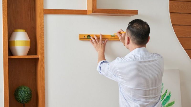 Мужчина отмеряет стену под крепеж полки в рыхлой стене