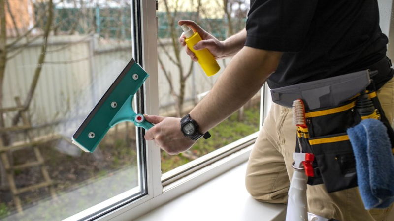 Мужчина отмывает окно от грязи и следов монтажной пены