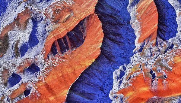 Вид с воздуха на живописный район Цицай Данся (или знаменитые Радужные горы) под падающим снегом в геопарке Чжанъе, провинция Ганьсу, Китай.