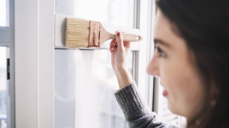 Девушка ведет малярную кисть по раме пластикового окна