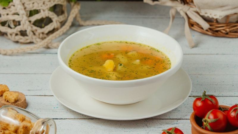 На столе стоит тарелка с ароматным и насыщенным куриным супом