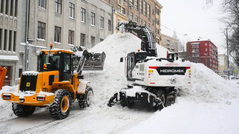 Трактор и экскаватор убирают снег во дворе жилого дома